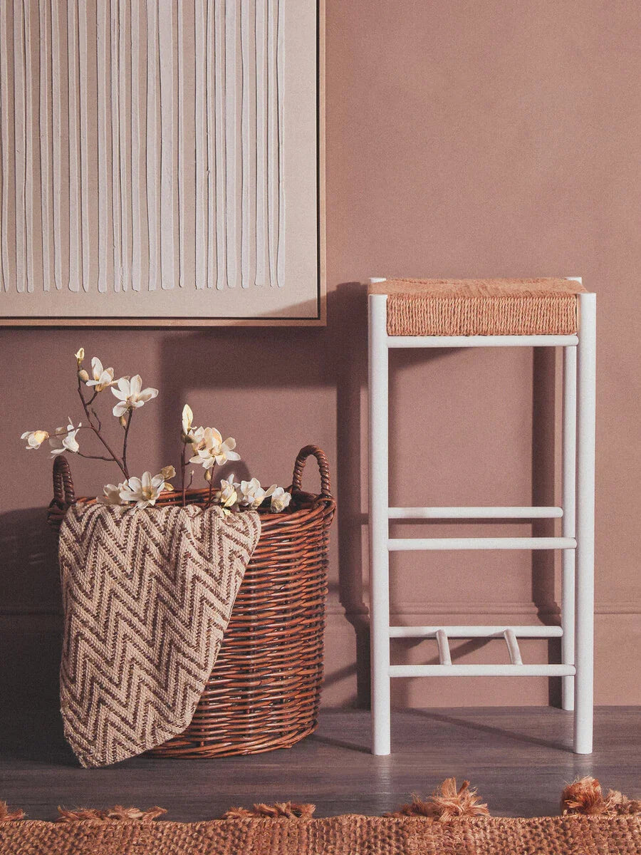 Woven basket with flowers and chevron throw beside a white and natural wood stool