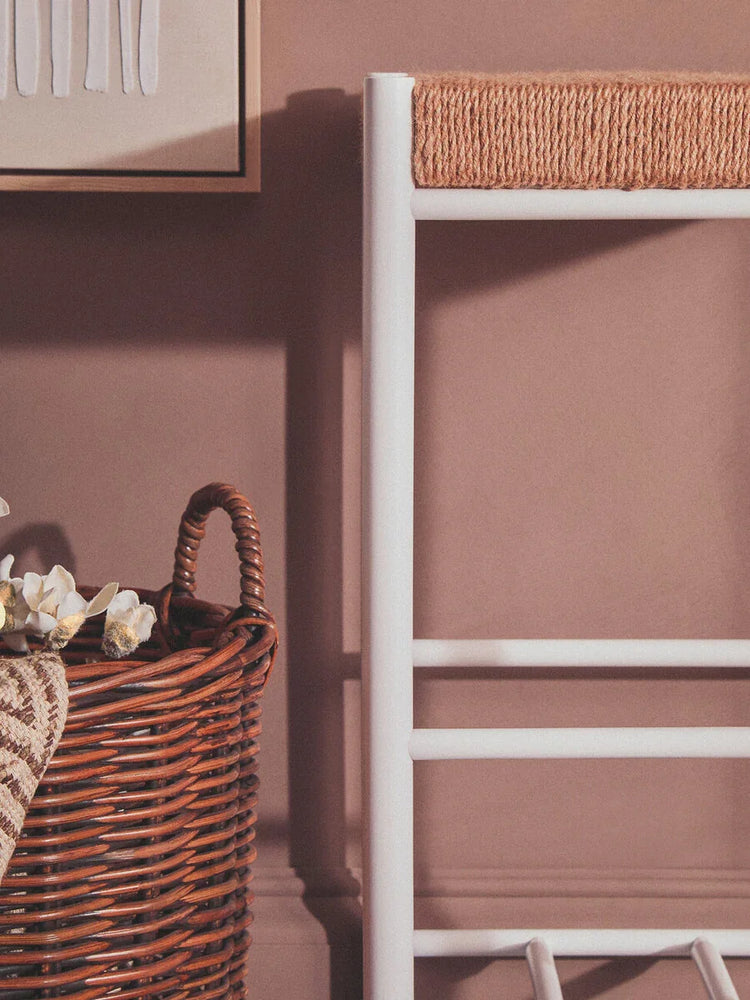 White towel ladder with rope detailing beside brown wicker storage basket and wall art