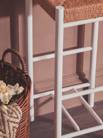 Bar stool with white metal legs and woven rattan seat beside wicker basket on wooden floor