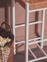 Bar stool with white metal legs and woven rattan seat beside wicker basket on wooden floor
