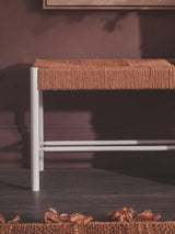 Woven bench with natural fibre seat and white metal legs against dark wall and floor