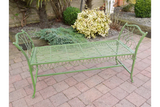 Green metal garden bench with decorative armrests on brick patio