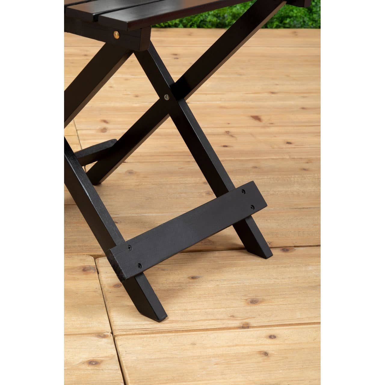 Black wood folding table with a sturdy X-shaped base, set against a wooden floor. The table features a smooth surface and clean lines, showcasing its minimalist design