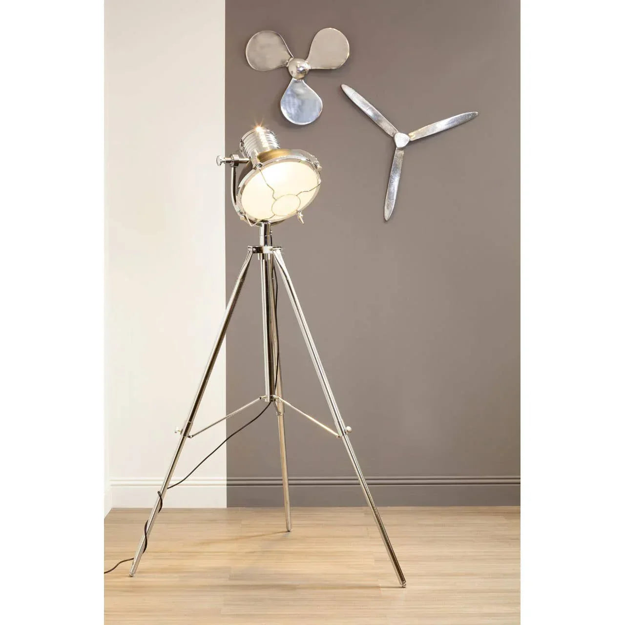 Chrome tripod floor lamp with spotlight head in modern room with metal wall art