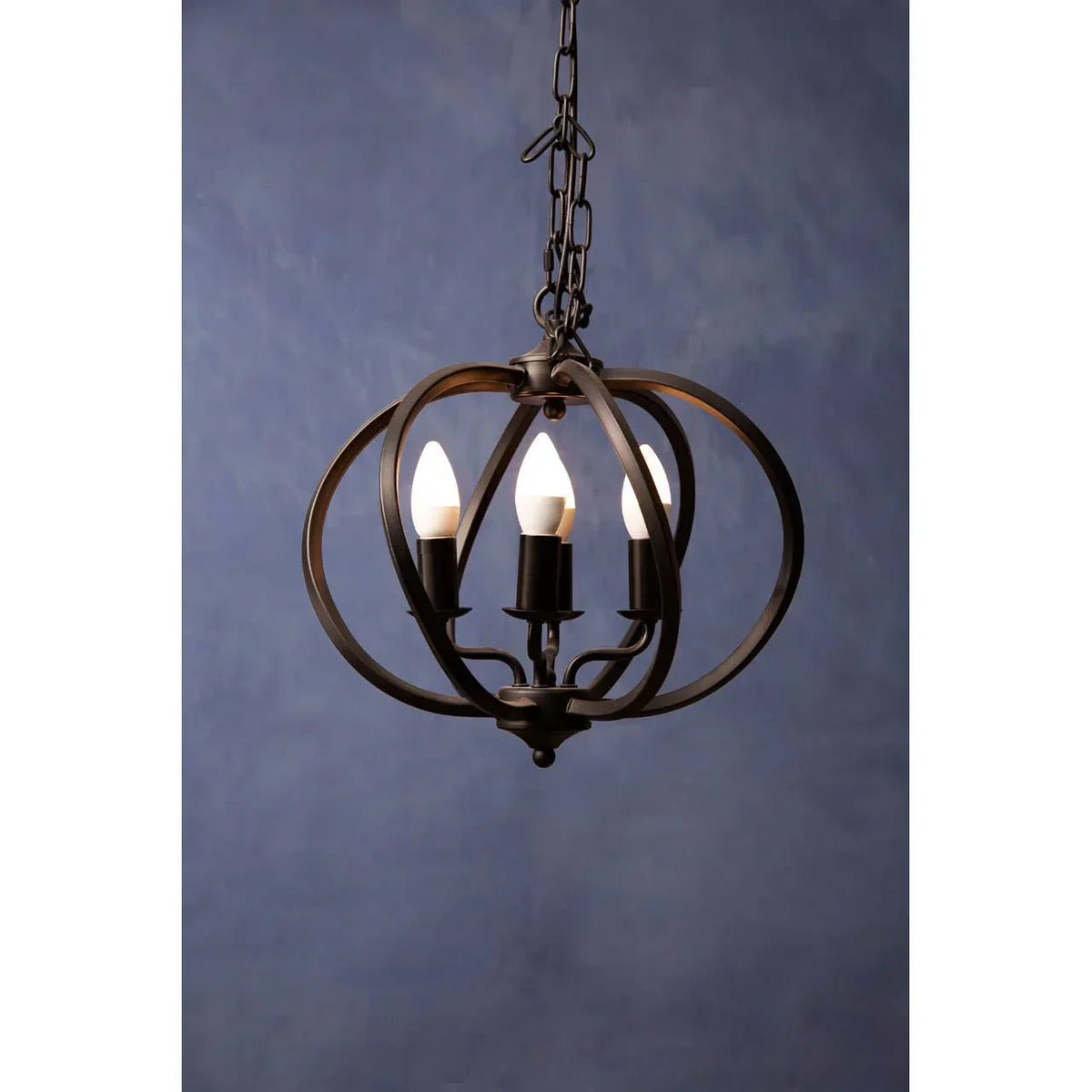 Black metal orb pendant light with three candle bulbs and chain hanging against blue wall