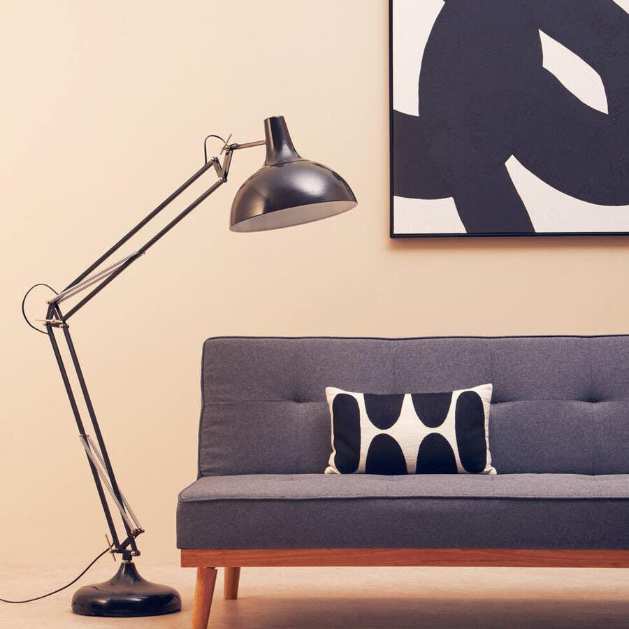 Grey fabric sofa with wooden legs, black floor lamp, abstract wall art and patterned cushion