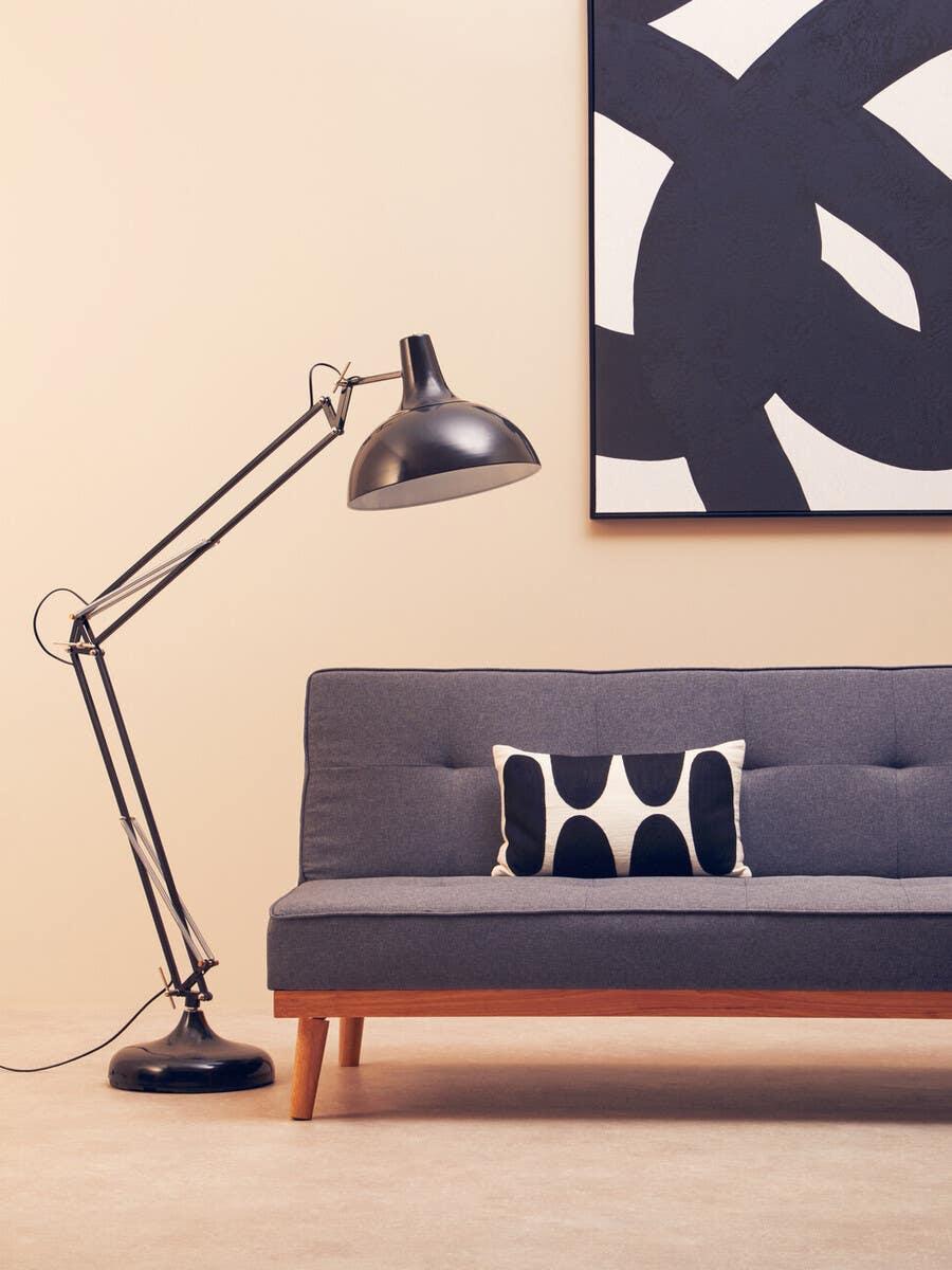 Grey fabric sofa with wooden legs, black floor lamp, abstract wall art and patterned cushion