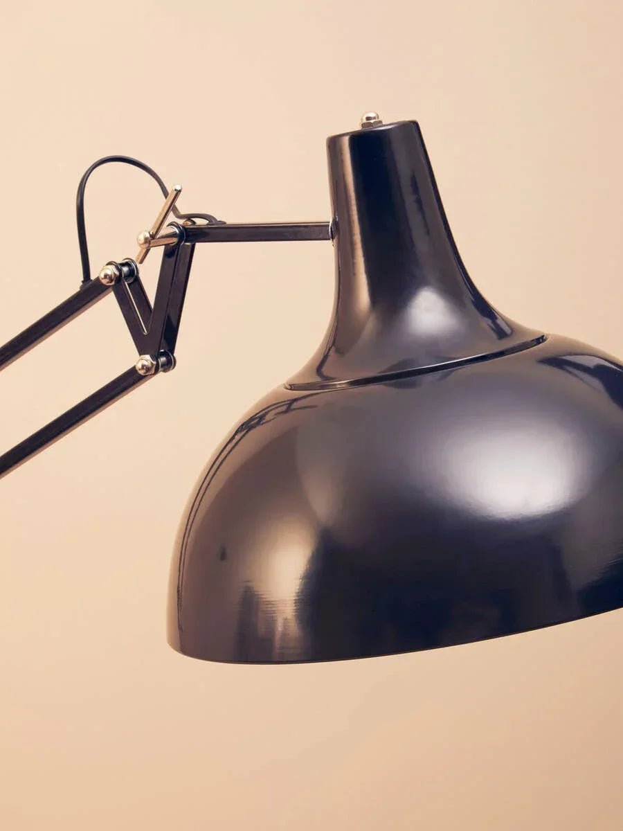 Black adjustable metal desk lamp with angled arm against a beige background