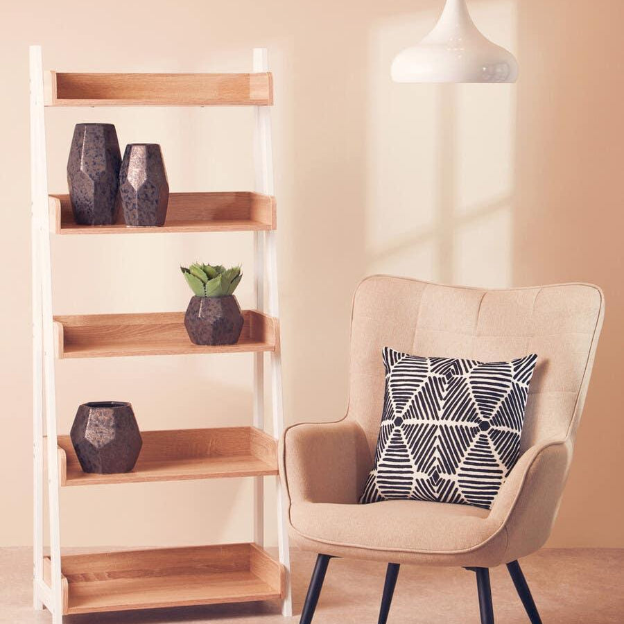 Beige accent chair with geometric cushion beside wooden shelving unit and pendant light