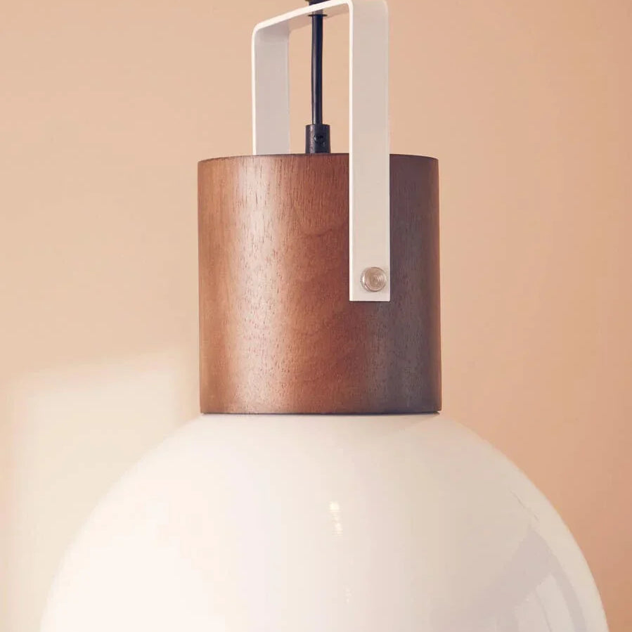 Modern ceiling pendant light with white glass shade and wood detail against beige wall