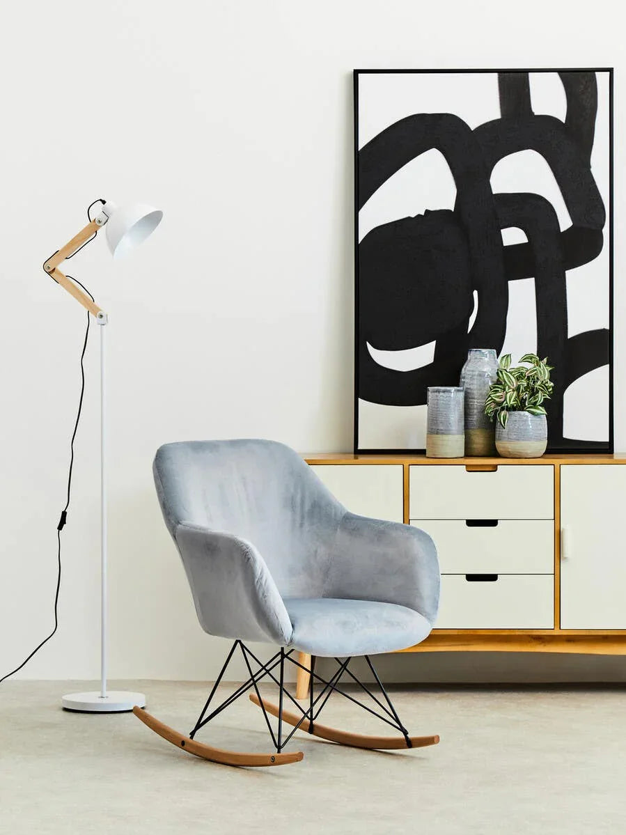 Grey velvet rocking chair beside wooden sideboard and modern floor lamp in living room