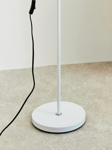 White floor lamp base with power cord on light stone flooring