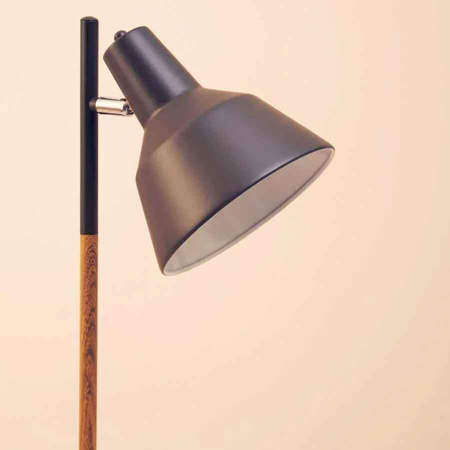 Black metal floor lamp with angled shade and wood effect stand against neutral wall