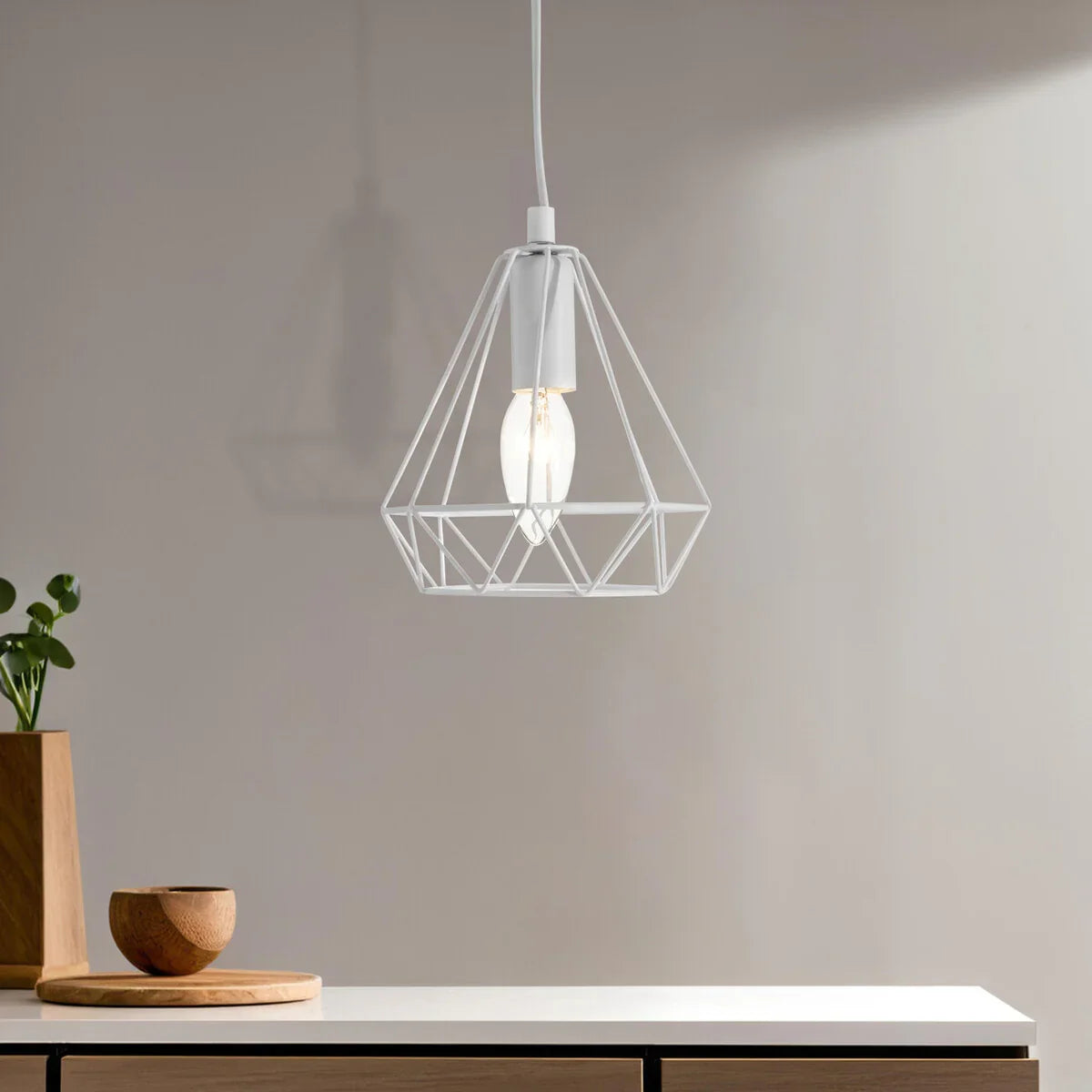 White geometric pendant light above modern table with wooden bowl and plant