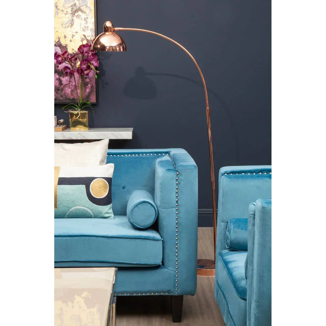 Blue velvet sofa with cushions beside copper arc floor lamp in living room