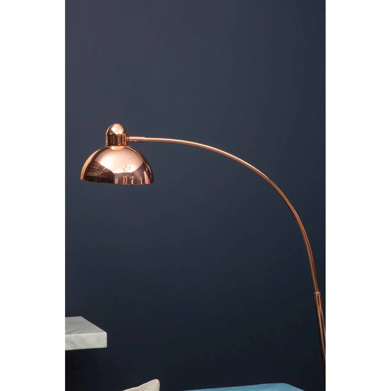 Copper arc floor lamp with dome shade against dark blue wall