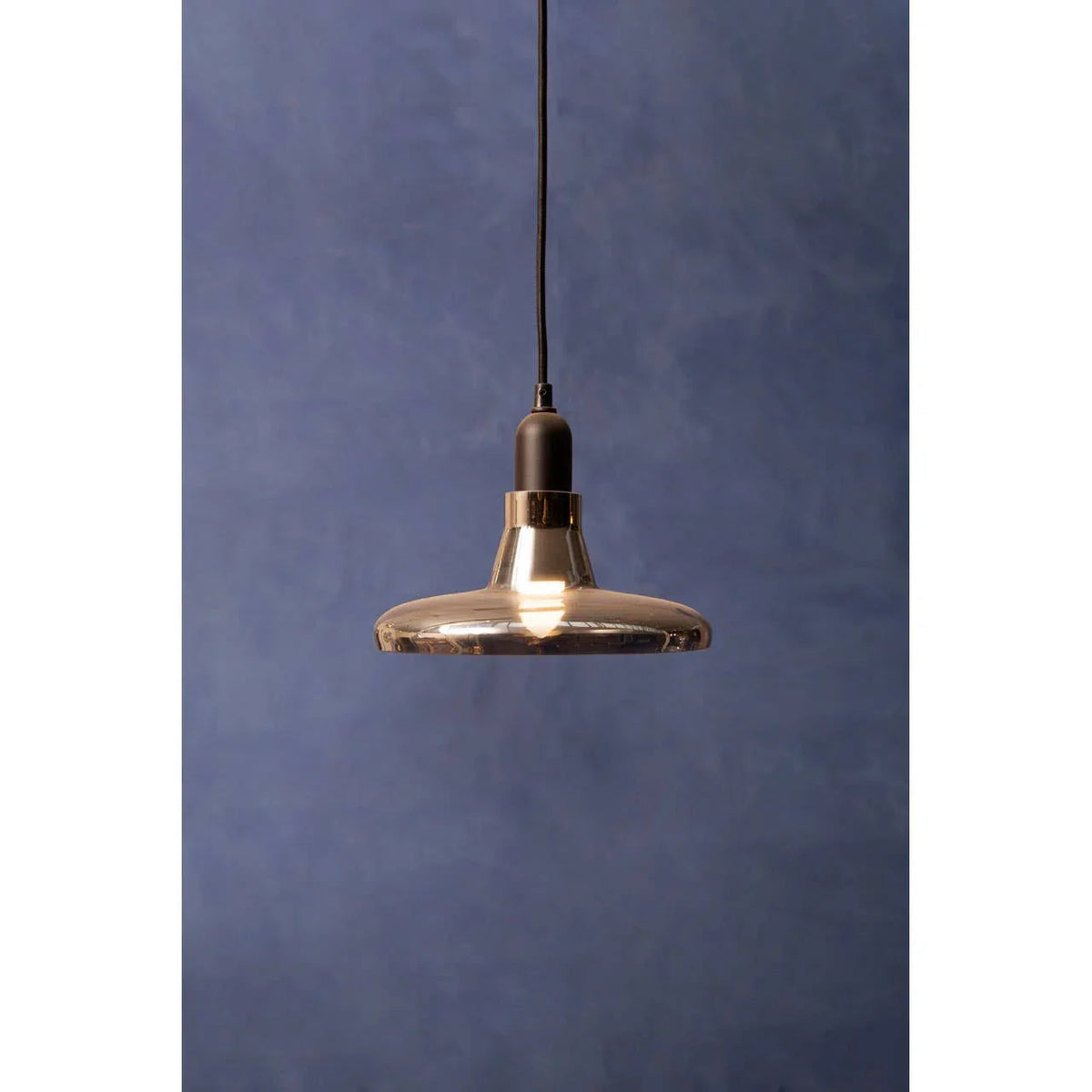 Amber glass plate-shaped pendant light, lit, against a dark blue wall