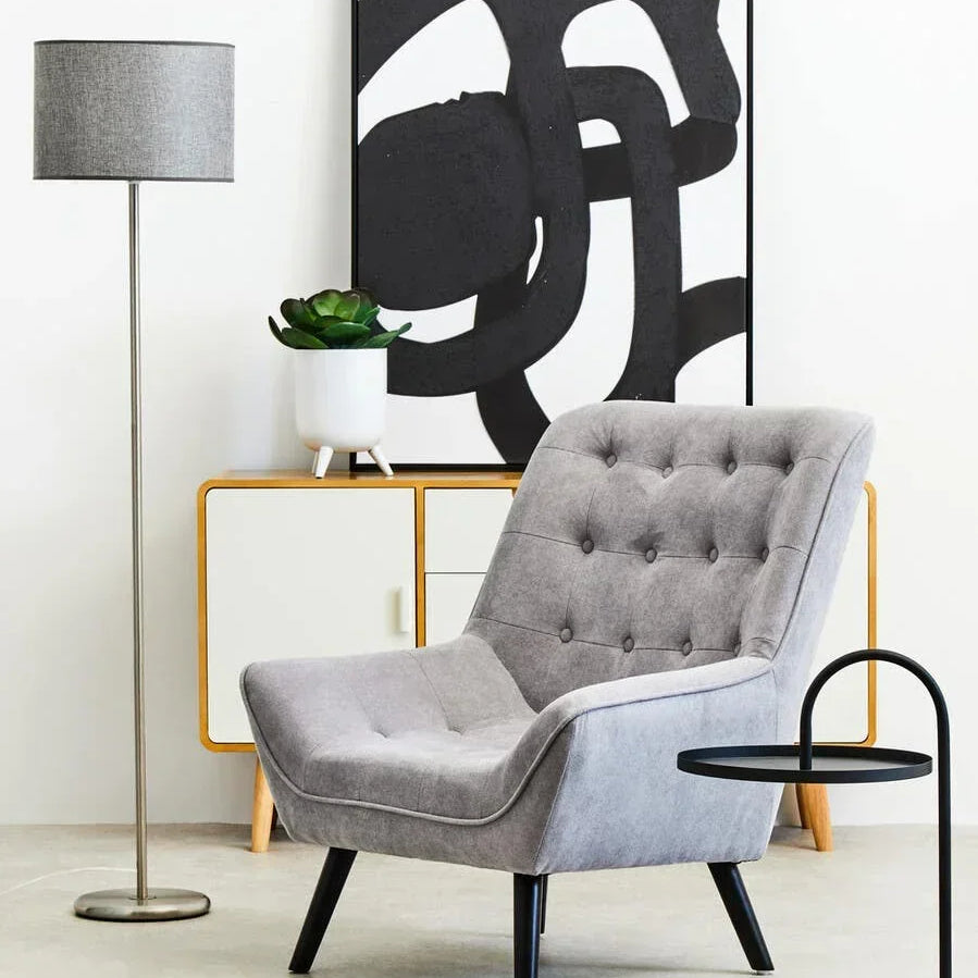 Grey accent armchair with button tufting, beside side table, lamp, and sideboard