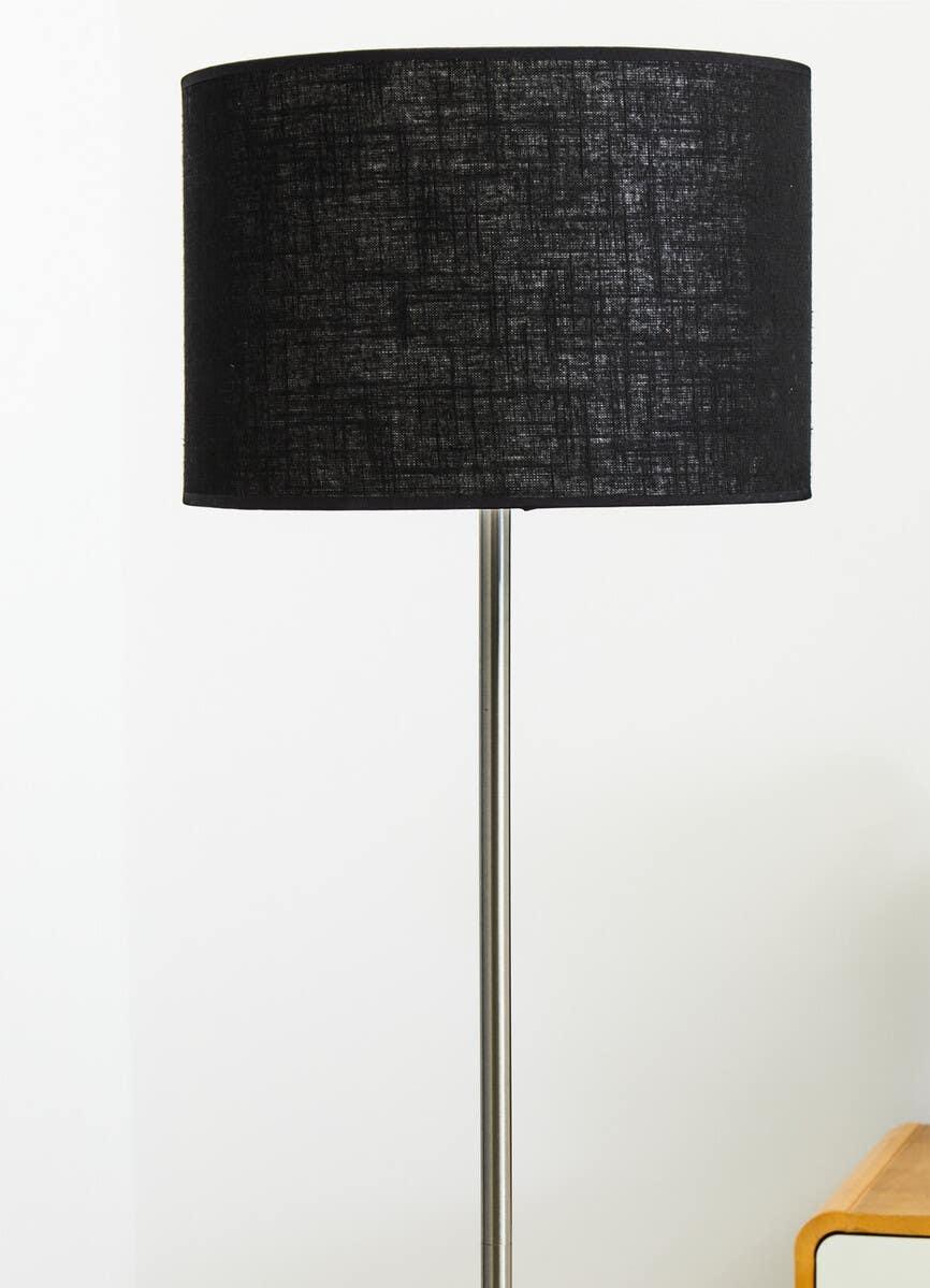 Black fabric floor lamp with chrome stand beside wooden table against white wall
