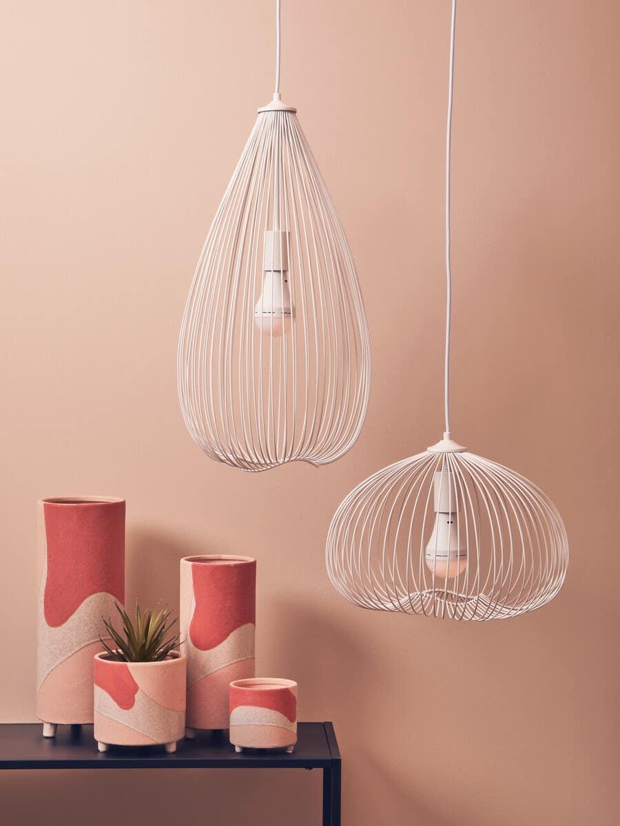White wire pendant lights above pink and beige ceramic plant pots on a black console table