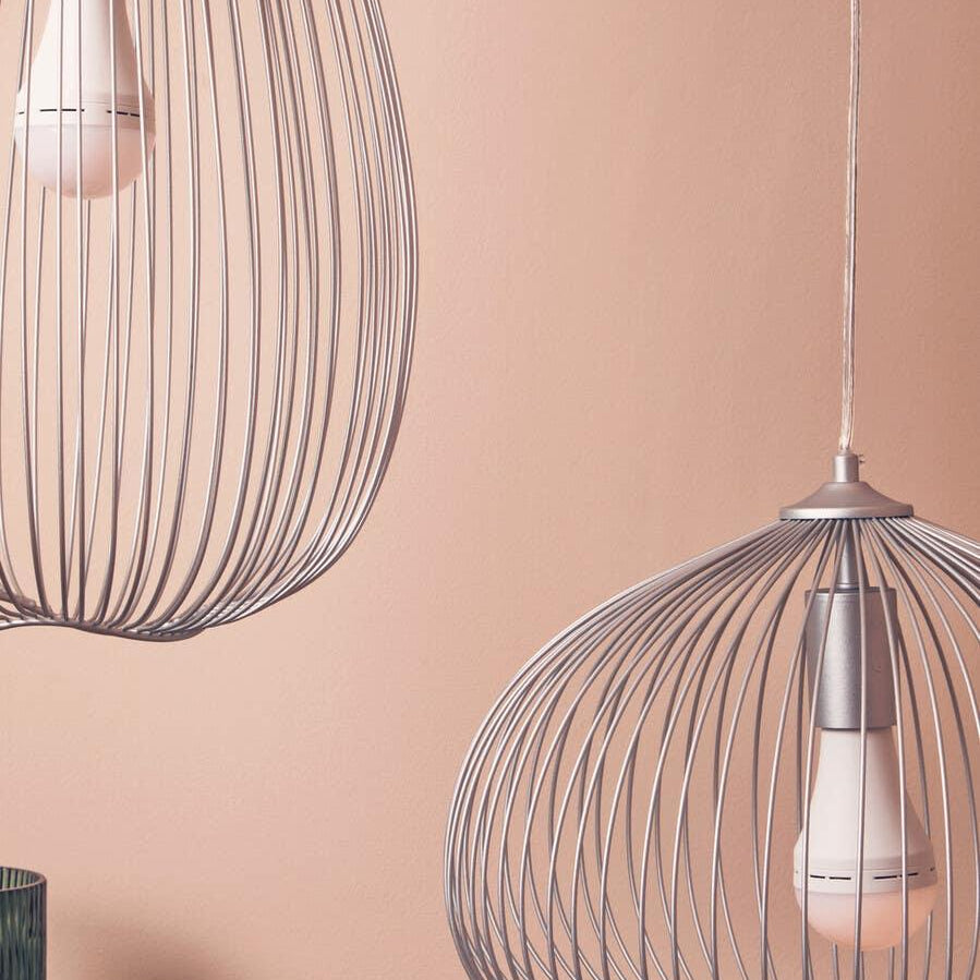 Pair of modern metal wire pendant lights with exposed bulbs against a peach wall