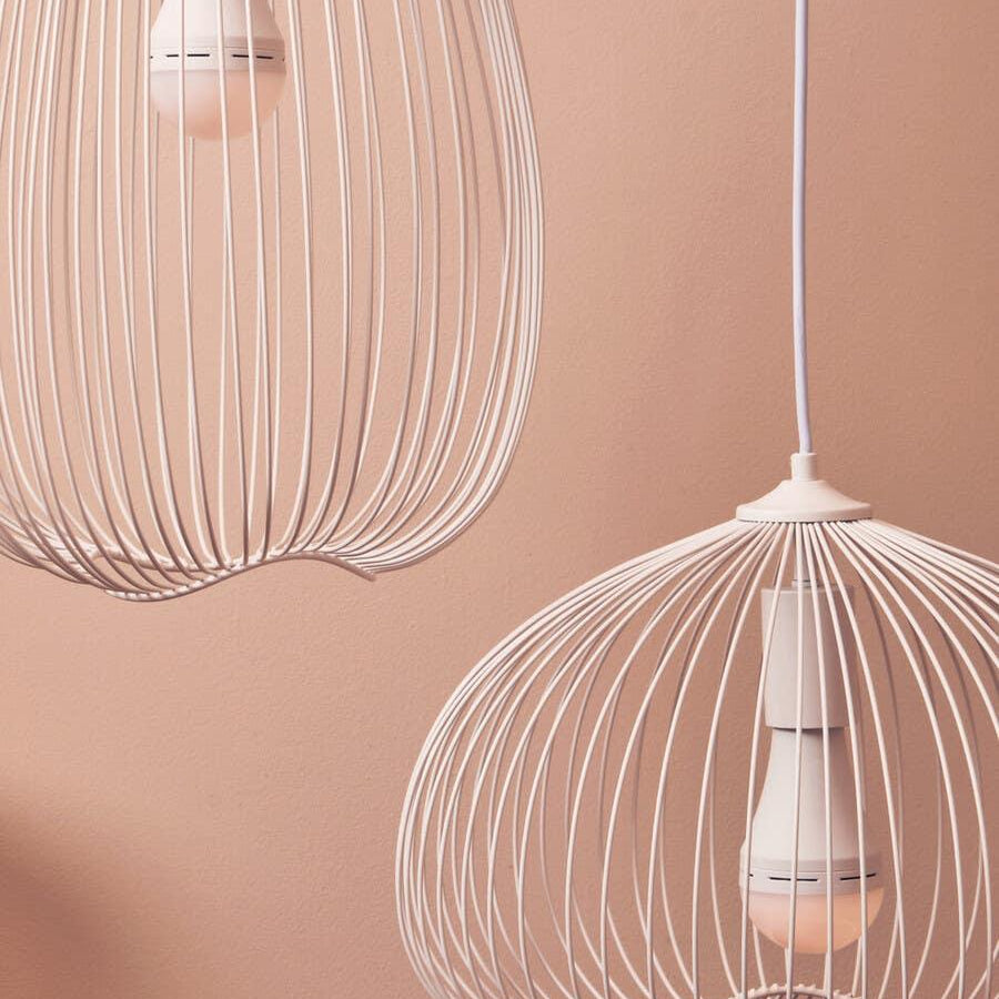 Modern pendant light fixtures with white wire frames and exposed bulbs against pink wall
