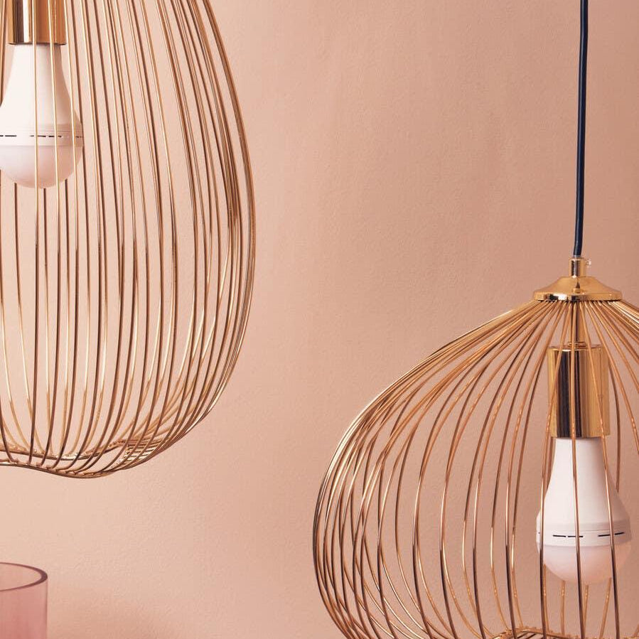 Gold wire pendant light shades with exposed bulbs against a soft pink wall