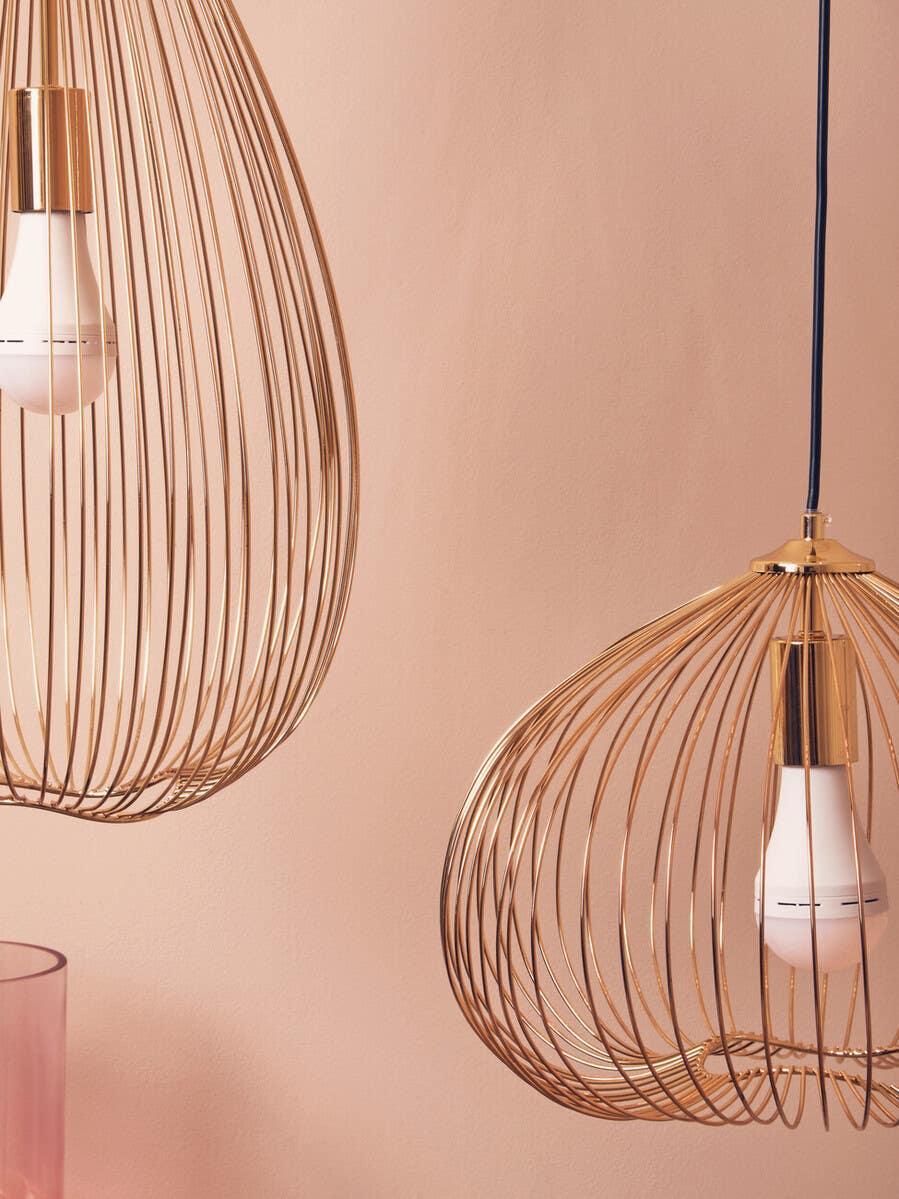 Gold wire pendant lights with exposed bulbs against a pale pink wall