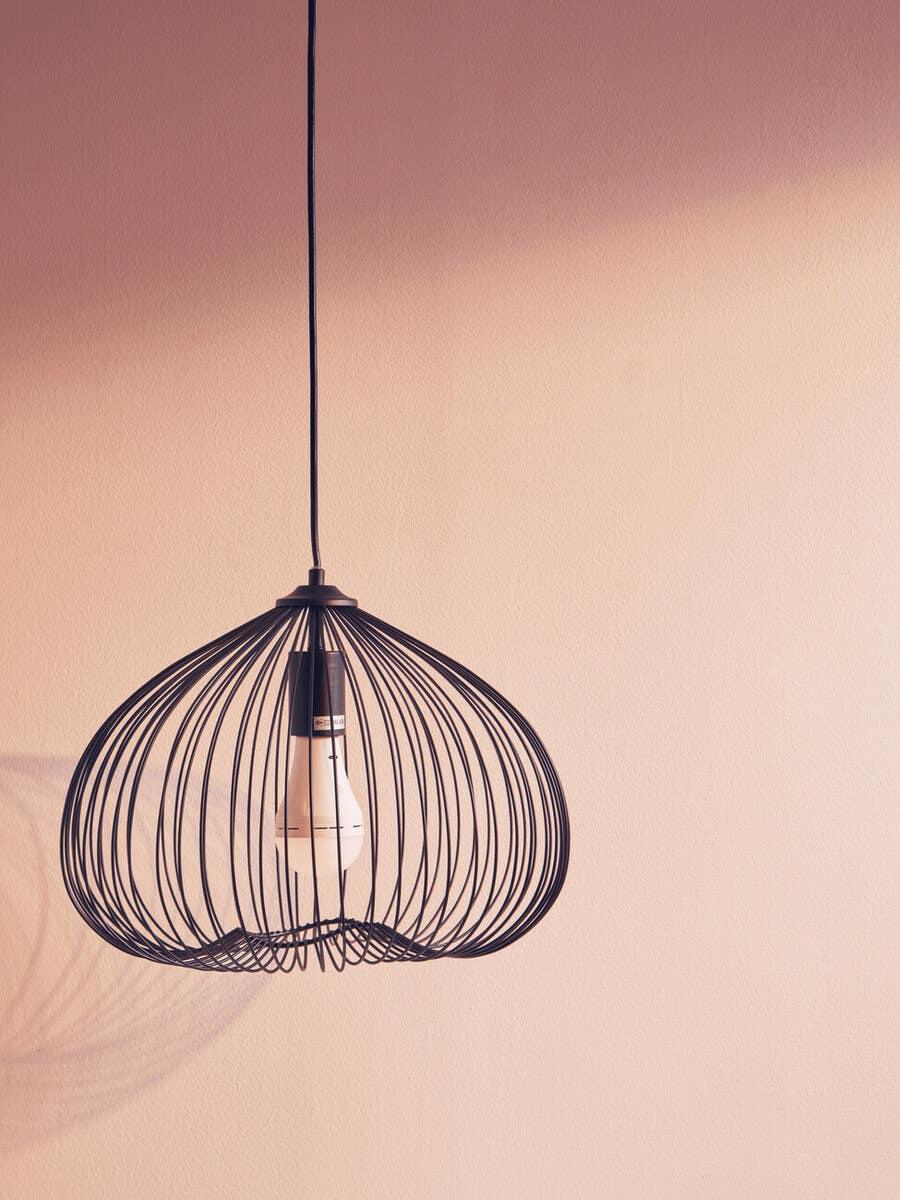 Black metal wire pendant light fixture with exposed bulb against beige wall