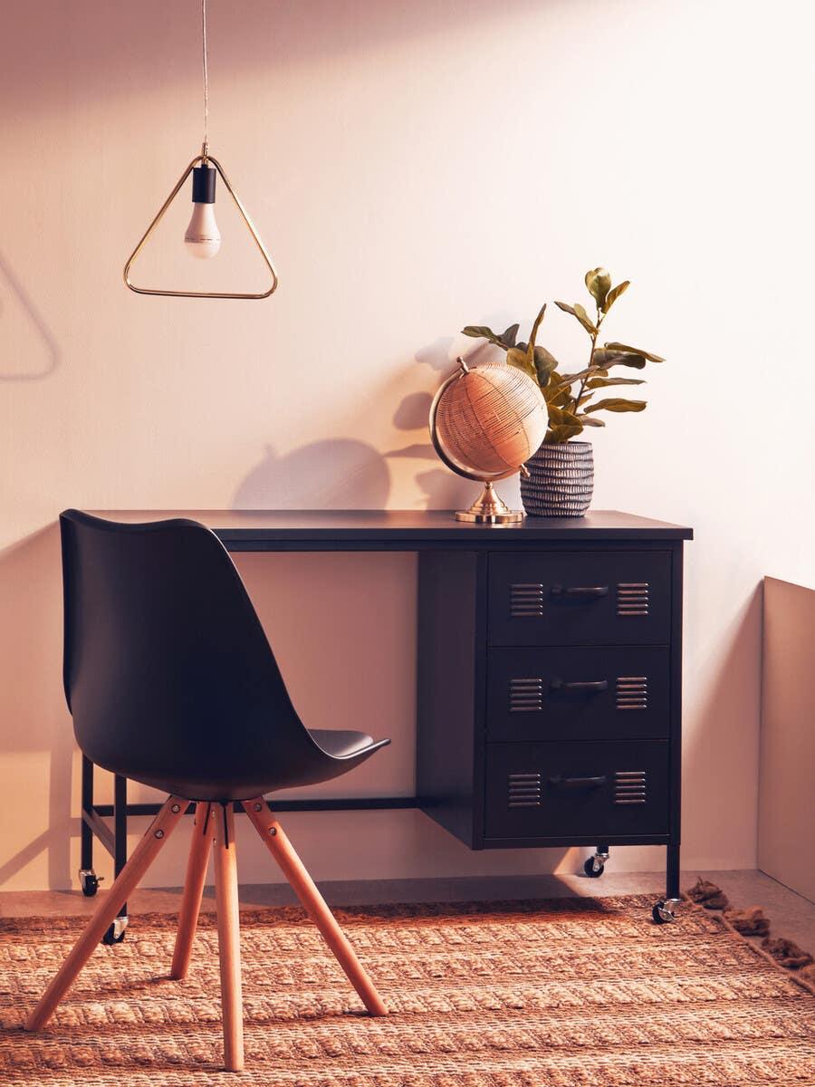 Black office desk with drawers, black chair, decorative globe, and plant on woven rug