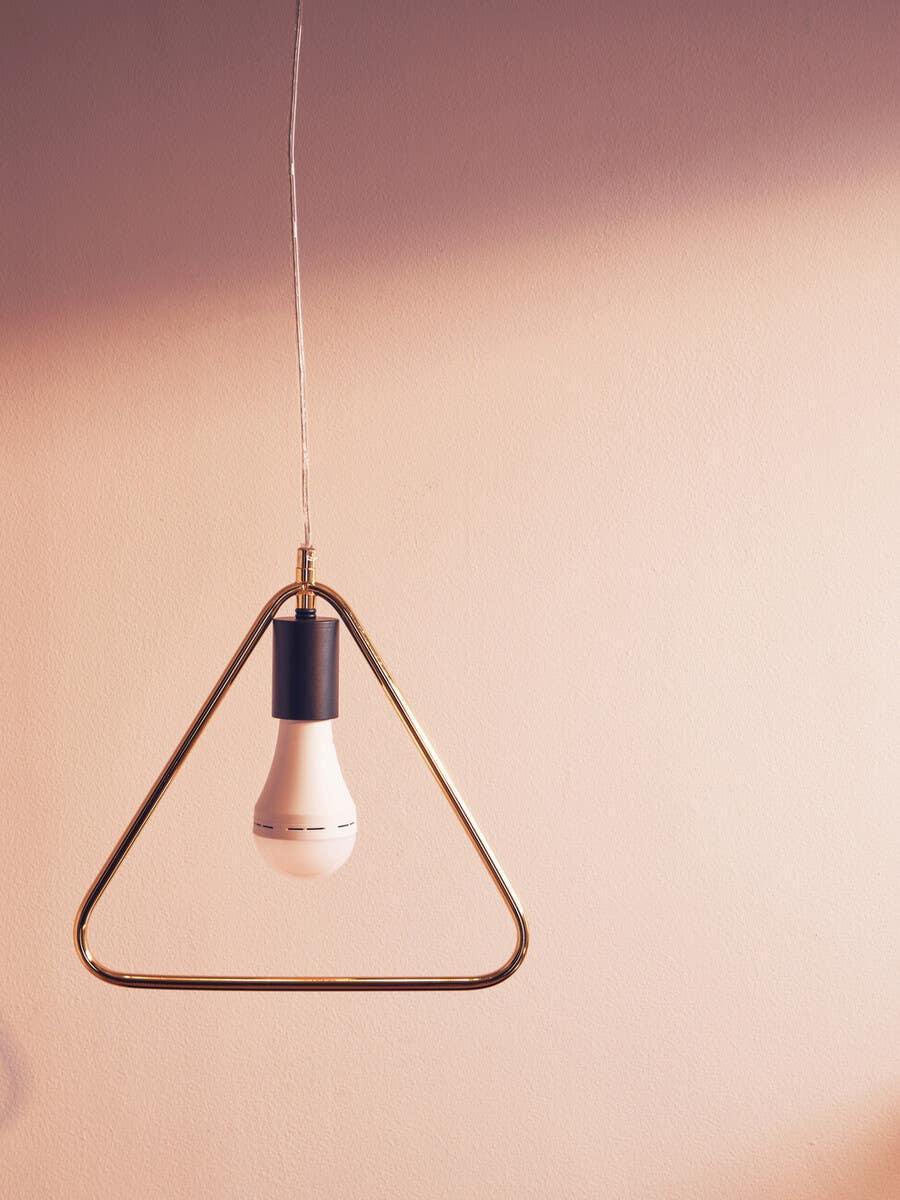 Modern pendant light with gold triangular frame and exposed bulb against beige wall