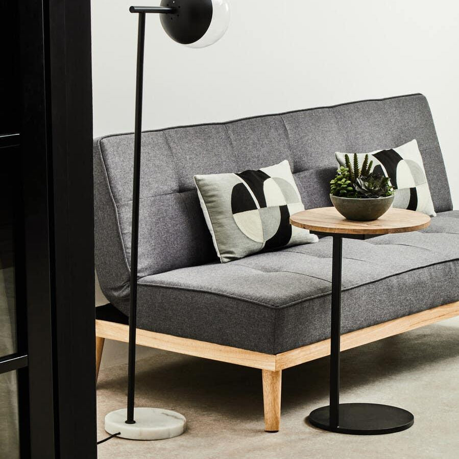 Grey fabric sofa with wooden legs, geometric cushions, round side table and modern floor lamp
