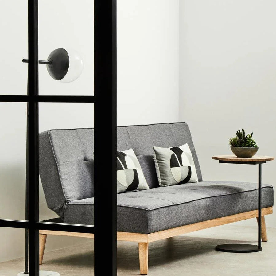 Grey fabric sofa with wooden legs, two geometric cushions, side table, and indoor plant