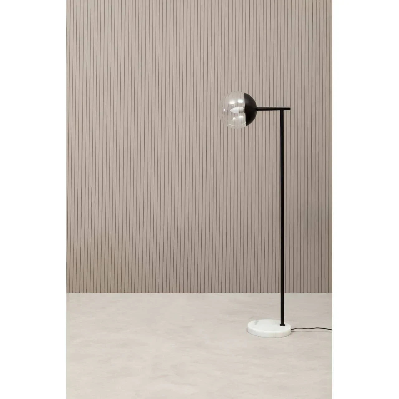 Black floor lamp with round glass shade and white base against striped beige wall