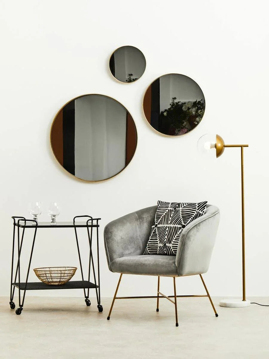 Grey velvet accent chair with gold legs, geometric cushion, bar cart, and round wall mirrors
