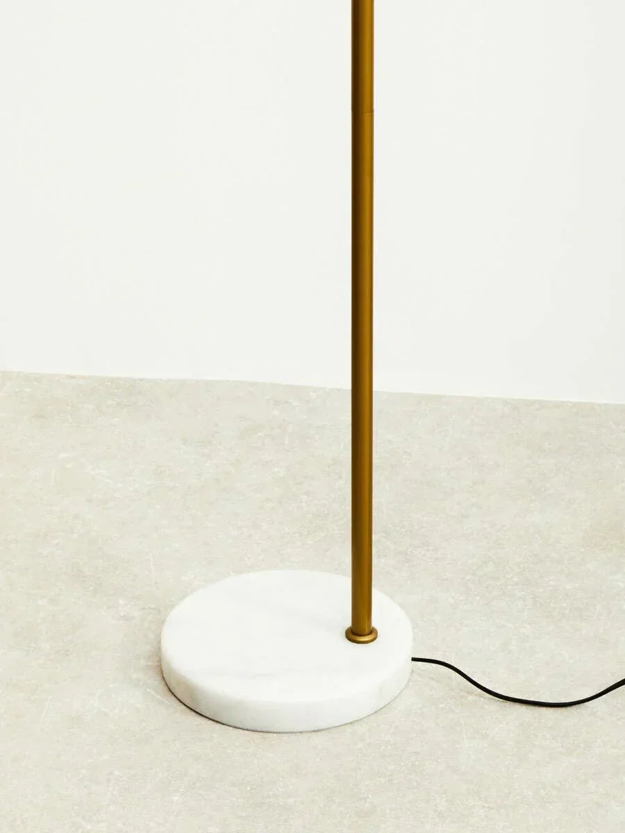 Gold floor lamp with marble base on light tile floor, power cord visible on side