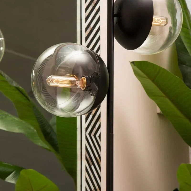 Modern floor lamp with black stem and clear glass globes beside large green indoor plants