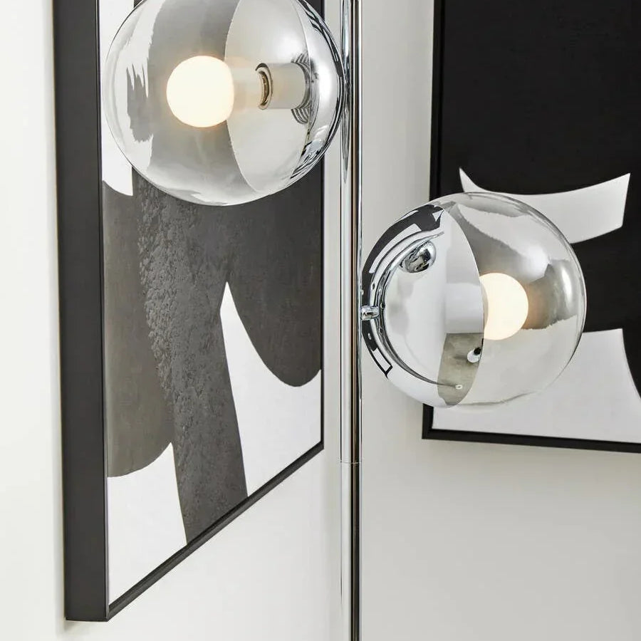 Chrome floor lamp with two glass globe shades beside abstract black and white wall art