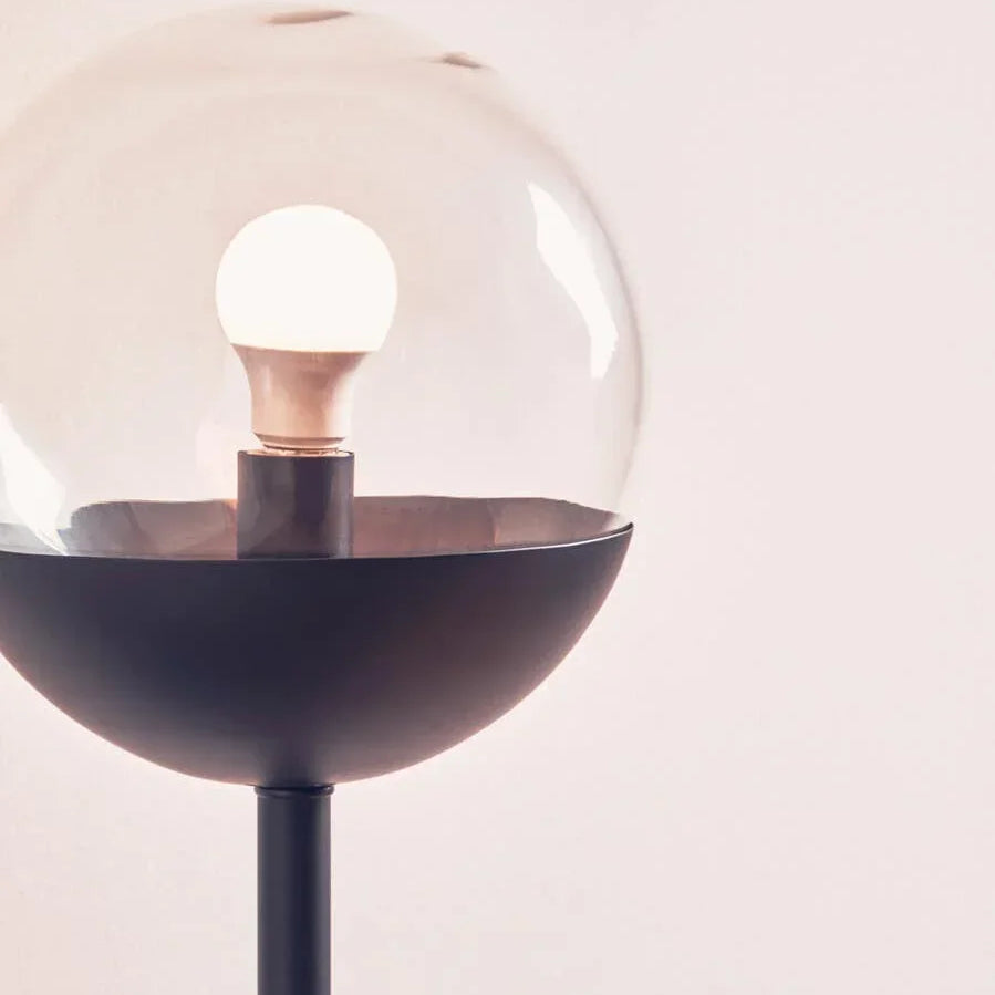 Modern floor lamp with round glass shade and black metal base against light wall