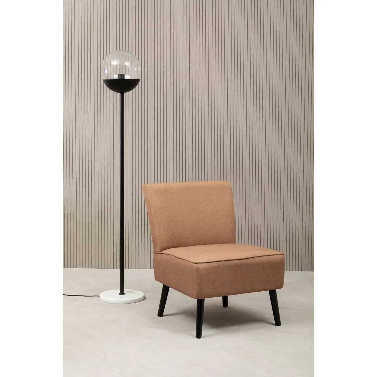 Tan fabric accent chair with black legs beside a modern floor lamp on light flooring