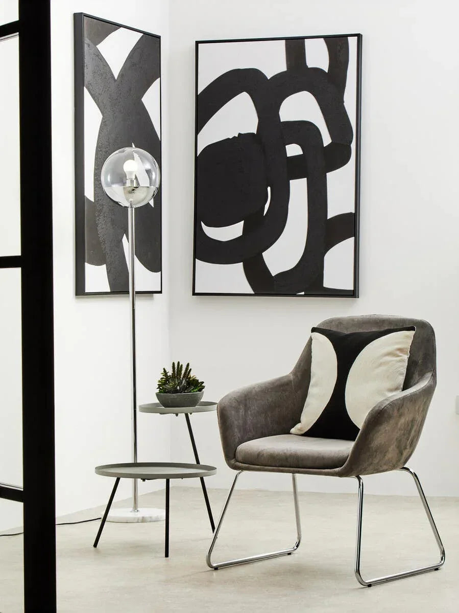 Modern grey accent chair with chrome legs, side tables, and black abstract wall art