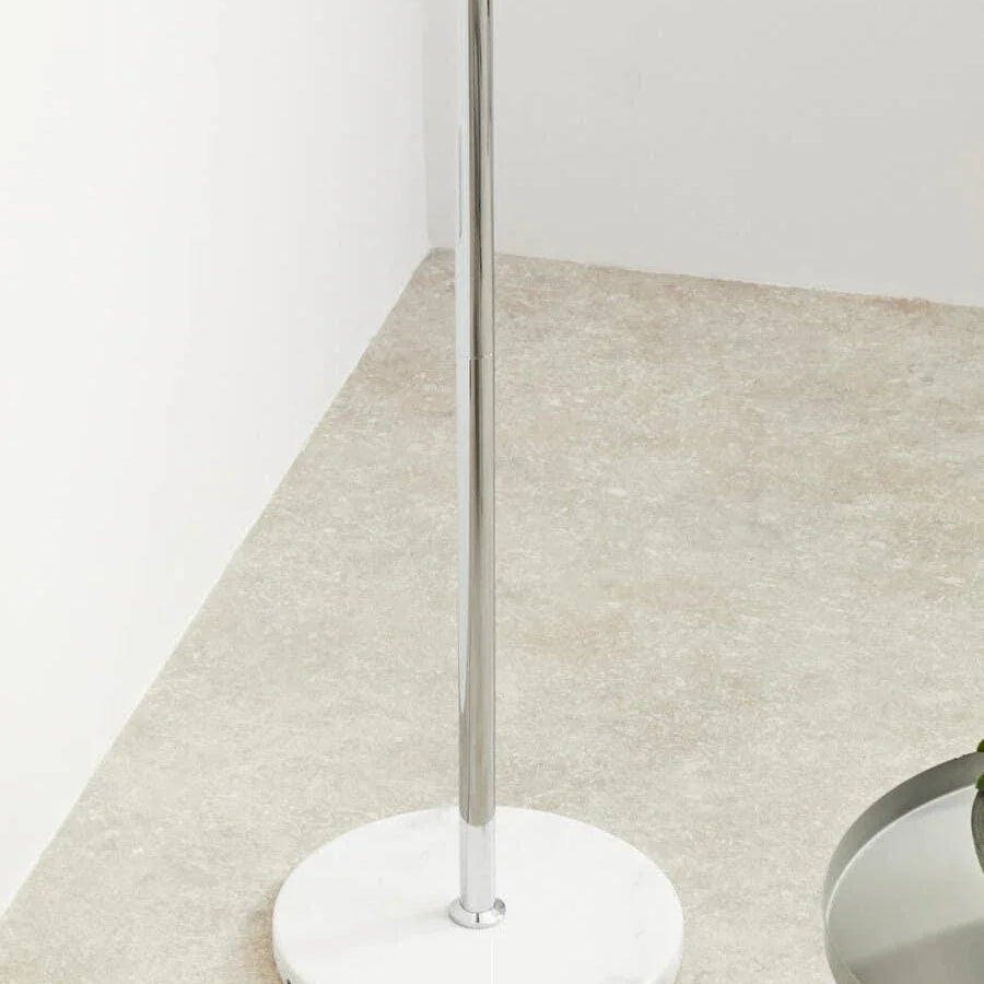 Chrome floor lamp with round marble base on light stone floor near a table edge