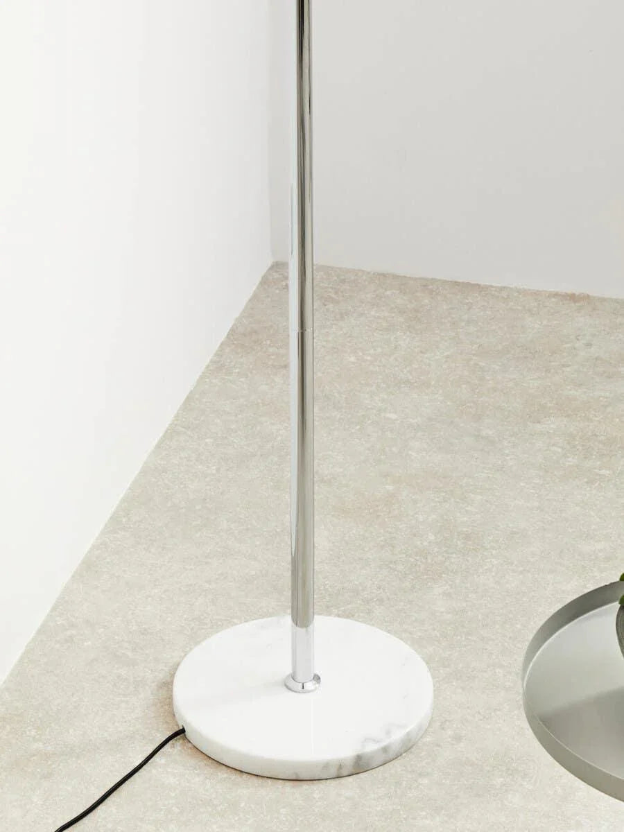 Chrome floor lamp with round marble base on light stone floor near a table edge