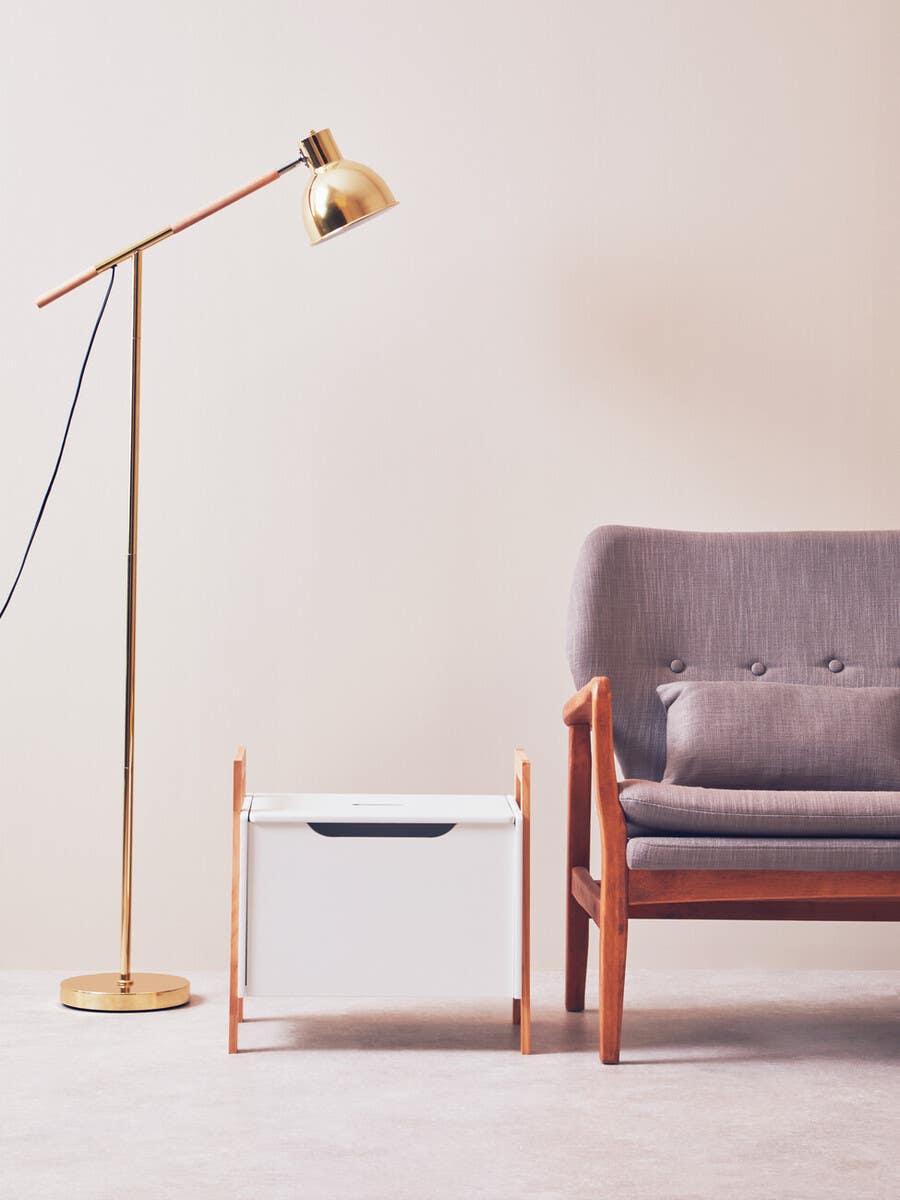 Grey upholstered armchair with wooden frame beside gold floor lamp and white storage box