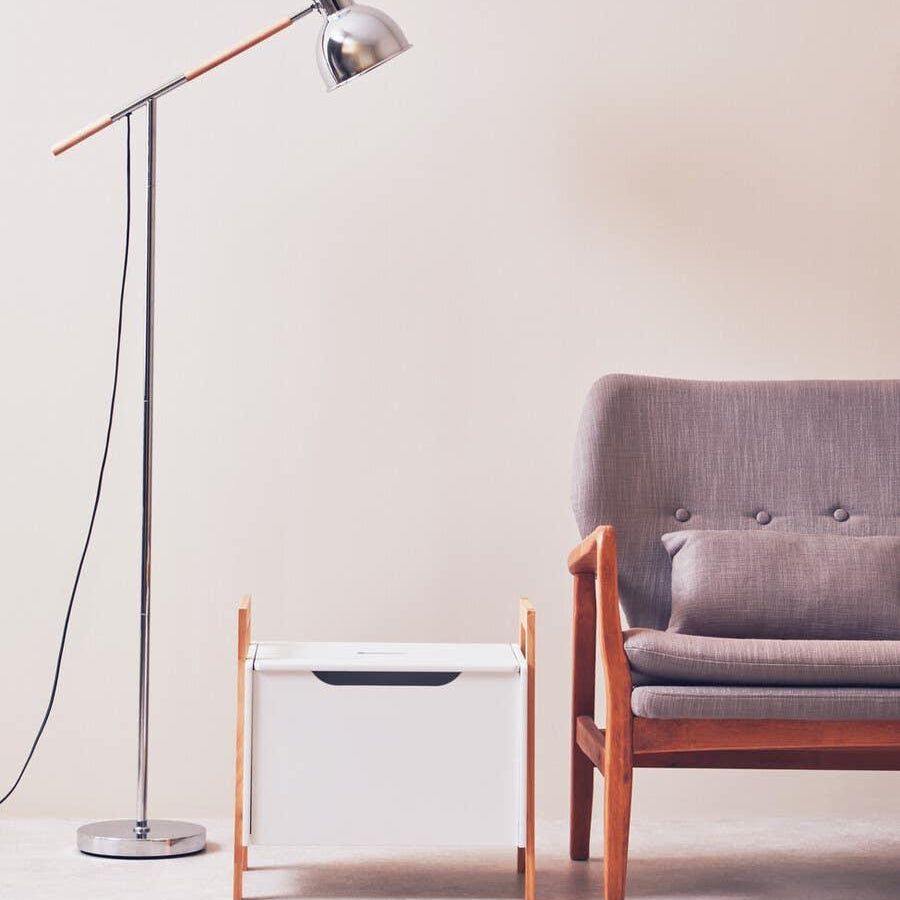Modern floor lamp beside grey cushioned armchair and white wooden storage box in living room