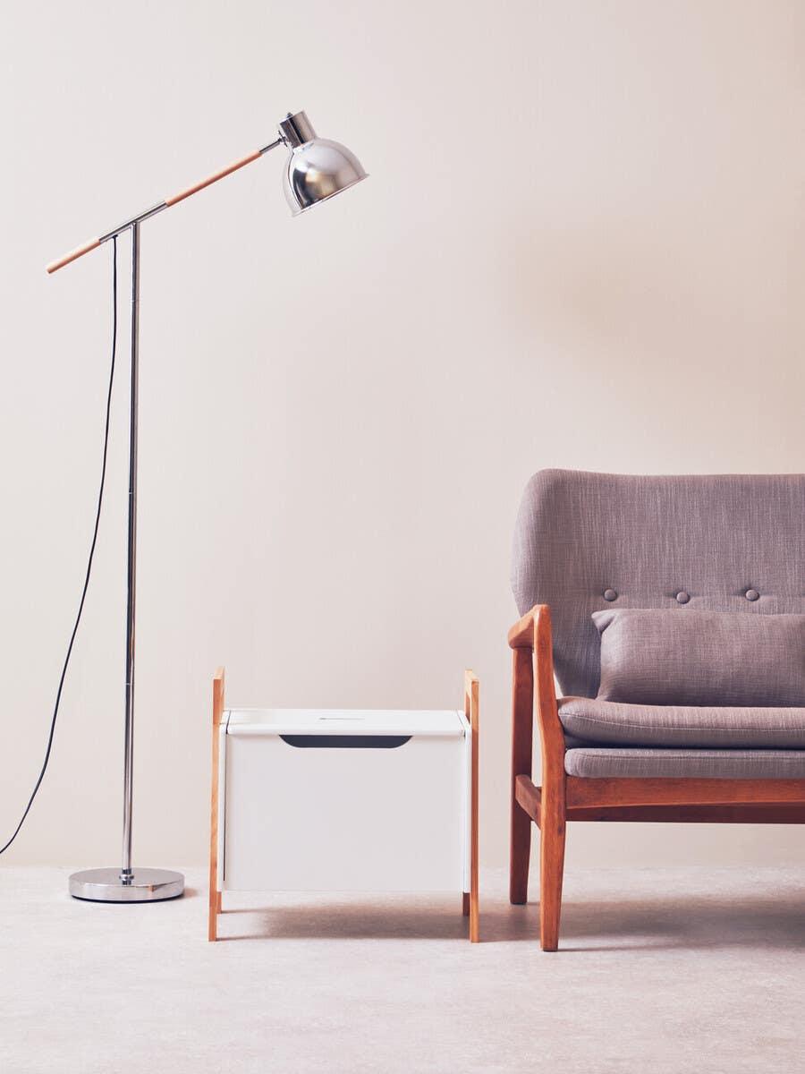 Modern floor lamp beside grey cushioned armchair and white wooden storage box in living room