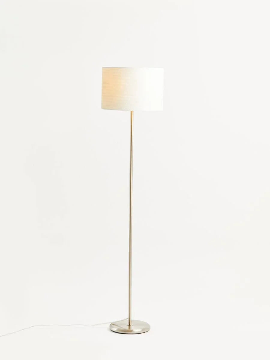 Modern floor lamp with white drum shade and brushed metal stand on white background