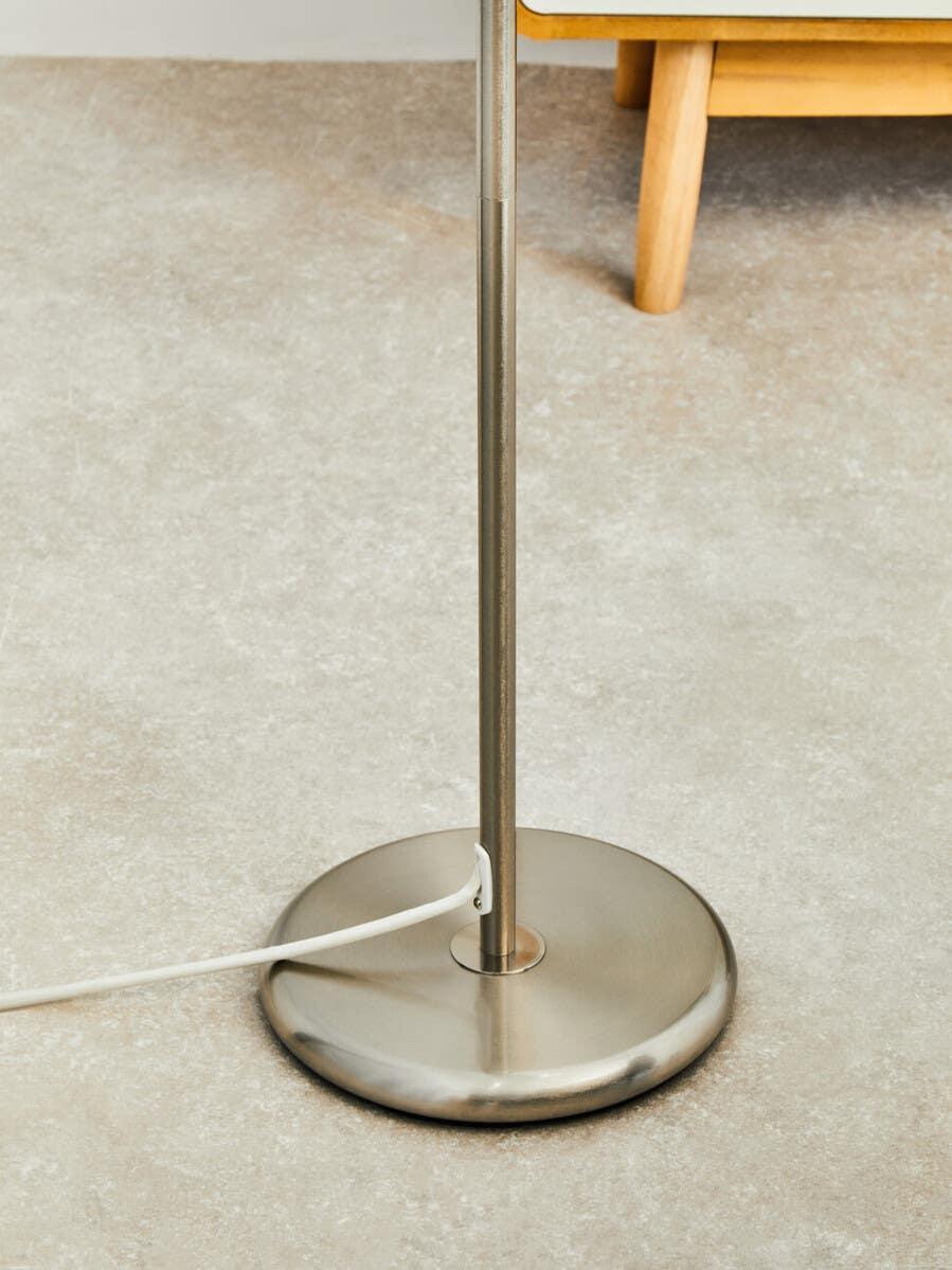 Brushed metal floor lamp base with power cord on stone-effect flooring