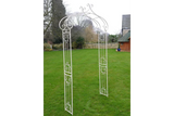 White metal garden arch with decorative scrollwork on lawn
