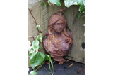 Cast iron garden wall art with woman's face mounted on wooden fence surrounded by ivy